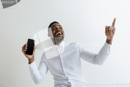 Image of Indoor portrait of attractive young black african man isolated on pink background, holding blank smartphone, smiling at camera, showing screen, feeling happy and surprised. Human emotions, facial