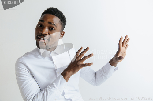 Image of Handsome Afro American man in classic shirt is smiling, looking at camera and pointing away, against white brick wall