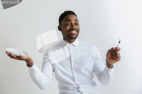 Image of Young smiling attractive african american guy holding empty dish and spoon isolated on grey background. Copy space and mock up. Blank template background.