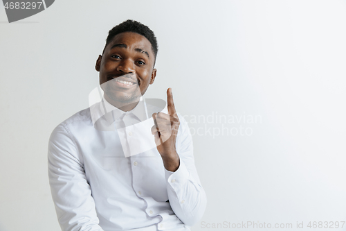 Image of Handsome Afro American man in classic shirt is smiling, looking at camera and pointing away, against white brick wall