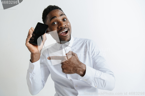 Image of Indoor portrait of attractive young black african man isolated on pink background, holding blank smartphone, smiling at camera, showing screen, feeling happy and surprised. Human emotions, facial