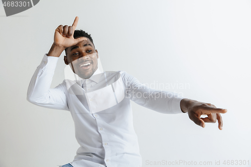 Image of Losers go home. Portrait of happy guy showing loser sign over forehead and smiling in cause of victory and laughing over gray background