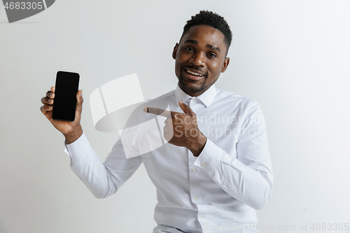 Image of Indoor portrait of attractive young black african man isolated on pink background, holding blank smartphone, smiling at camera, showing screen, feeling happy and surprised. Human emotions, facial