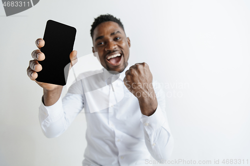 Image of Indoor portrait of attractive young black african man isolated on pink background, holding blank smartphone, smiling at camera, showing screen, feeling happy and surprised. Human emotions, facial