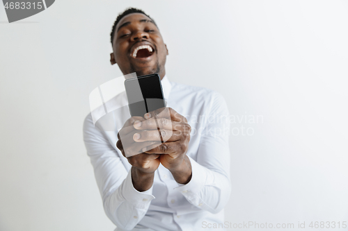 Image of Indoor portrait of attractive young black african man isolated on pink background, holding blank smartphone, smiling at camera, showing screen, feeling happy and surprised. Human emotions, facial