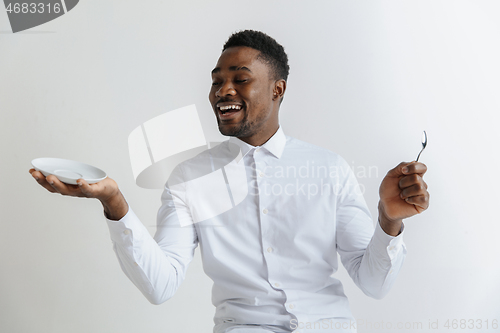 Image of Young smiling attractive african american guy holding empty dish and spoon isolated on grey background. Copy space and mock up. Blank template background.