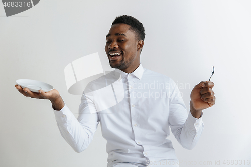 Image of Young smiling attractive african american guy holding empty dish and spoon isolated on grey background. Copy space and mock up. Blank template background.