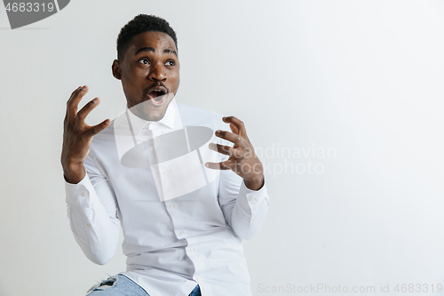 Image of Wow. Attractive male half-length front portrait on grey studio backgroud. Young afro emotional surprised bearded man standing with open mouth. Human emotions, facial expression concept.