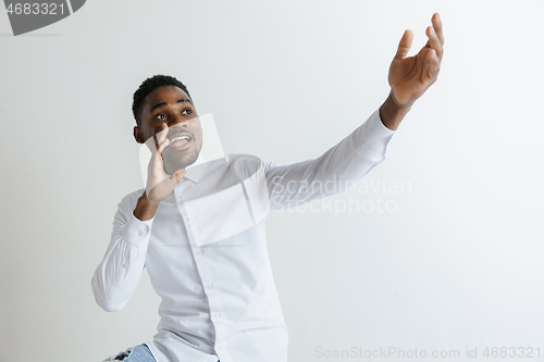 Image of Handsome Afro American man in classic shirt is smiling, looking at camera and pointing away, against white brick wall