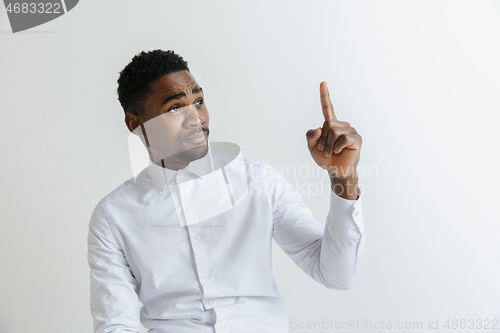 Image of Handsome Afro American man in classic shirt is smiling, looking at camera and pointing away, against white brick wall