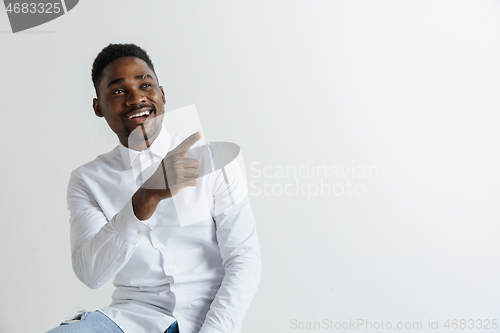 Image of Handsome Afro American man in classic shirt is smiling, looking at camera and pointing away, against white brick wall