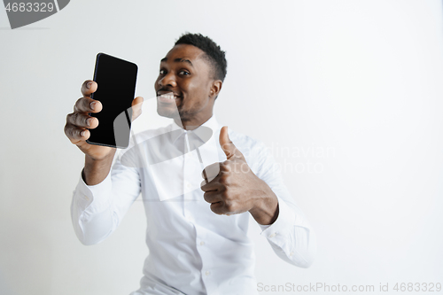 Image of Indoor portrait of attractive young black african man isolated on pink background, holding blank smartphone, smiling at camera, showing screen, feeling happy and surprised. Human emotions, facial