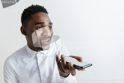 Image of Indoor portrait of attractive young black african man isolated on gray background, holding blank smartphone, using voice control, feeling happy and surprised. Human emotions, facial expression concep