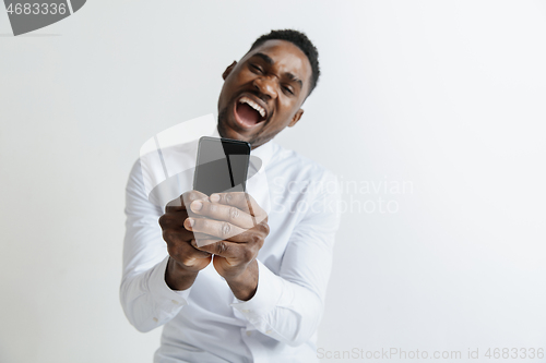 Image of Indoor portrait of attractive young black african man isolated on pink background, holding blank smartphone, smiling at camera, showing screen, feeling happy and surprised. Human emotions, facial