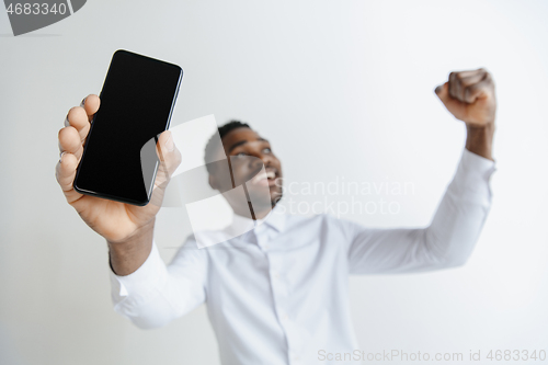 Image of Indoor portrait of attractive young black african man isolated on pink background, holding blank smartphone, smiling at camera, showing screen, feeling happy and surprised. Human emotions, facial