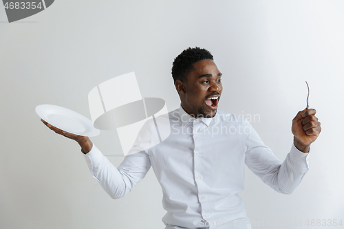 Image of Young happy african american guy holding empty dish and fork isolated on grey background. Copy space and mock up. Blank template background.