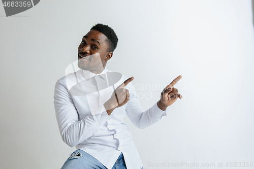 Image of Handsome Afro American man in classic shirt is smiling, looking at camera and pointing away, against white brick wall