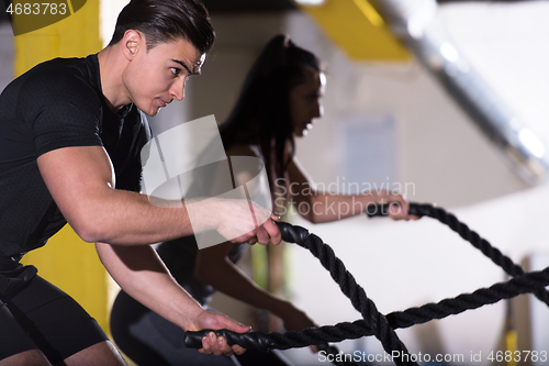 Image of sports couple doing battle ropes cross fitness exercise