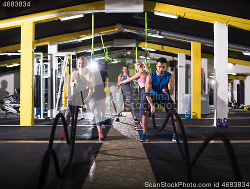 Image of sports couple doing battle ropes cross fitness exercise