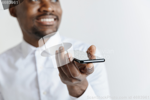 Image of Indoor portrait of attractive young black african man isolated on gray background, holding blank smartphone, using voice control, feeling happy and surprised. Human emotions, facial expression concep