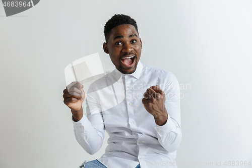 Image of Young afro man with a surprised happy expression won a bet on gray studio background. Human facial emotions and betting concept.