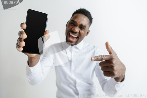 Image of Indoor portrait of attractive young black african man isolated on pink background, holding blank smartphone, smiling at camera, showing screen, feeling happy and surprised. Human emotions, facial