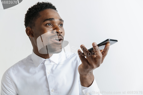 Image of Indoor portrait of attractive young black african man isolated on gray background, holding blank smartphone, using voice control, feeling happy and surprised. Human emotions, facial expression concep