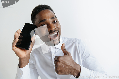 Image of Indoor portrait of attractive young black african man isolated on pink background, holding blank smartphone, smiling at camera, showing screen, feeling happy and surprised. Human emotions, facial