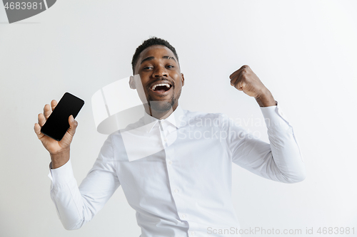 Image of Indoor portrait of attractive young black african man isolated on pink background, holding blank smartphone, smiling at camera, showing screen, feeling happy and surprised. Human emotions, facial