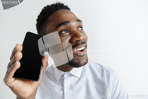 Image of Indoor portrait of attractive young black african man isolated on pink background, holding blank smartphone, smiling at camera, showing screen, feeling happy and surprised. Human emotions, facial