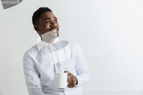 Image of Coffee makes his day. Young handsome African man drinking coffee and looking away while sitting at his working place