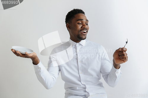 Image of Young smiling attractive african american guy holding empty dish and spoon isolated on grey background. Copy space and mock up. Blank template background.