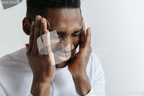 Image of Stressed young african american man having terrible strong headache.