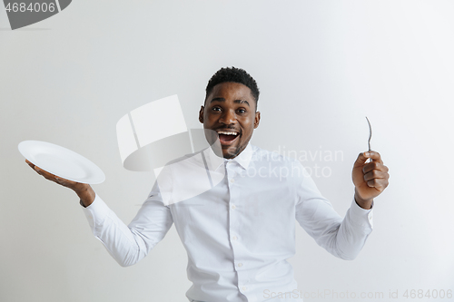 Image of Young happy african american guy holding empty dish and fork isolated on grey background. Copy space and mock up. Blank template background.