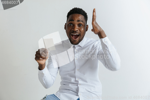 Image of Young afro man with a surprised happy expression won a bet on gray studio background. Human facial emotions and betting concept.