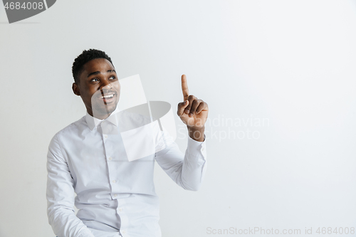 Image of Handsome Afro American man in classic shirt is smiling, looking at camera and pointing away, against white brick wall