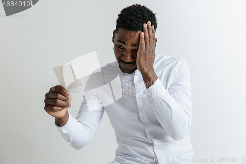 Image of Young afro man with a disappointed unhappy sad expression lost a bet on gray studio background. Human facial emotions and betting concept.