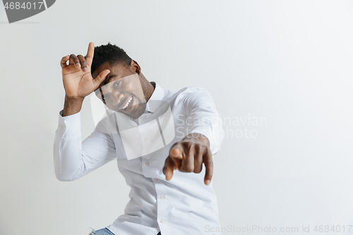 Image of Losers go home. Portrait of happy guy showing loser sign over forehead and smiling in cause of victory and laughing over gray background