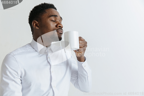 Image of Coffee makes his day. Young handsome African man drinking coffee and looking away while sitting at his working place