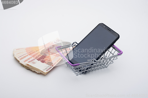 Image of Next to a stack of five thousandth bills is a grocery basket with a cell phone