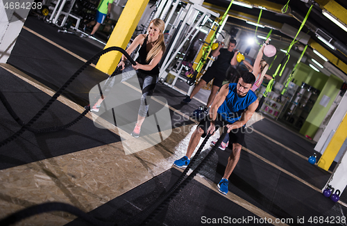 Image of sports couple doing battle ropes cross fitness exercise