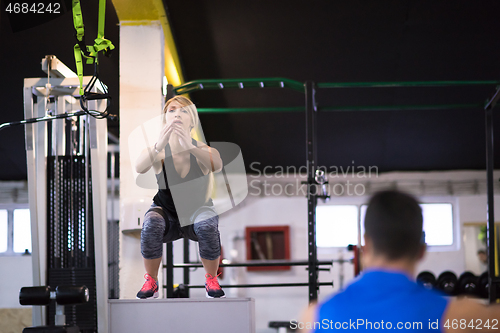 Image of woman working out with personal trainer jumping on fit box