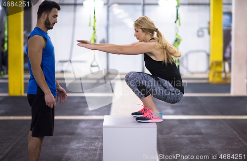 Image of woman working out with personal trainer jumping on fit box