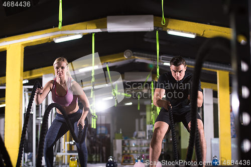 Image of sports couple doing battle ropes cross fitness exercise