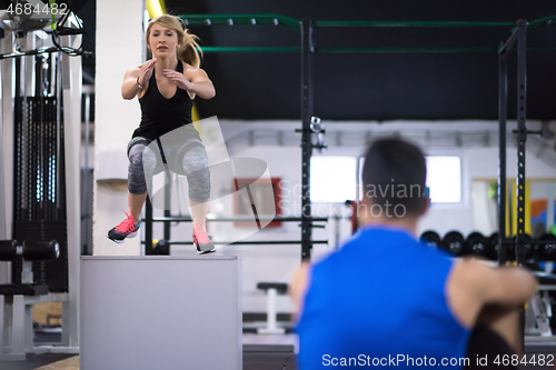 Image of woman working out with personal trainer jumping on fit box