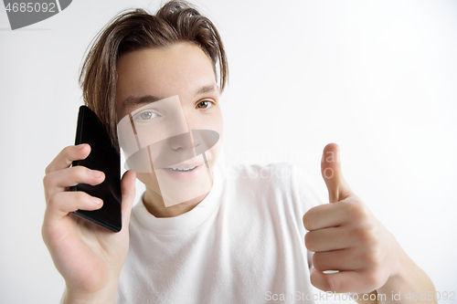 Image of Young handsome teenager showing smartphone screen and signing OK isolated on gray background