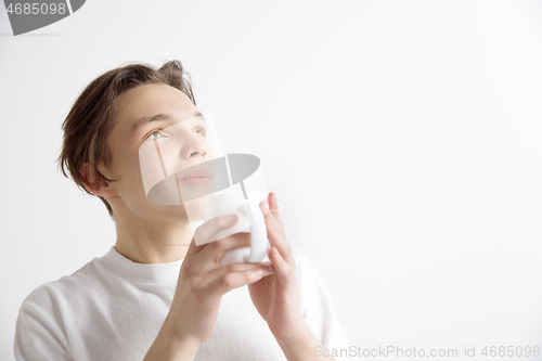 Image of Taking a coffee break. Handsome young man holding coffee cup, smiling while standing against gray background
