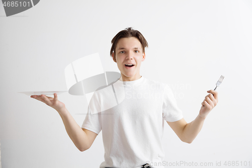 Image of Young smiling attractive guy holding empty dish and fork isolated on grey background.