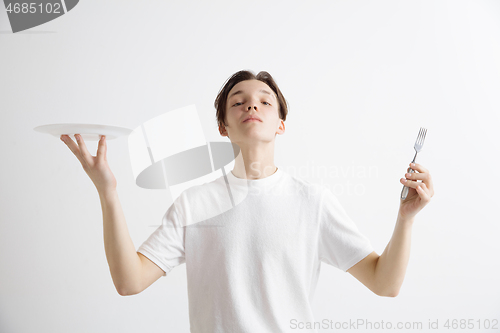 Image of Young smiling attractive guy holding empty dish and fork isolated on grey background.