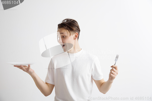 Image of Young smiling attractive guy holding empty dish and fork isolated on grey background.